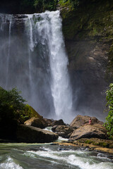 Obraz premium beautiful girl in bikini standing in front of large waterfall in costa rica; huge tropical waterfall