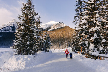 Mother and son walking along a snowy path at Lake Louise on a sunny winter morning.