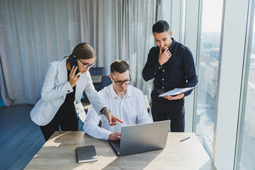 Group of business people in casual clothes talking to each other in office and using gadgets while working on business startup in modern workspace