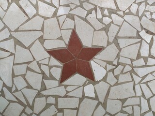 Red star design isolated on interior floor decorated with white broken or cracked waste ceramic or mosaic tile pieces. Old vintage architecture tiling art background texture pattern. Closeup view.