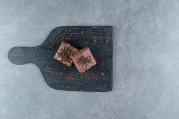Two small pieces of brownie on a dark plate