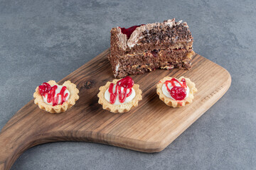 A piece of tasty cake and mini cupcakes on a wooden board