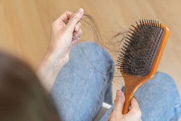 Serious asian young woman, girl hand in holding comb, show her hairbrush with long loss hair...