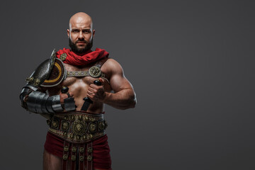 Portrait of bearded gladiator dressed in armor and red cloak holding two swords.