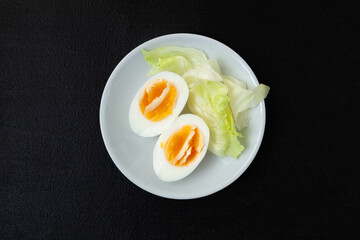 Halves of a hard-boiled chicken egg with lettuce greens on a plate on a dark background