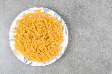 Plate of raw fusilli on marble surface