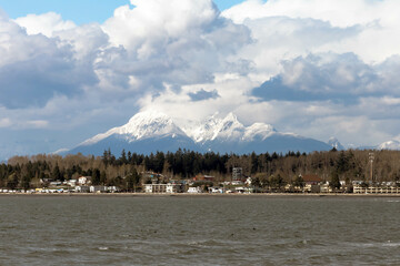 Wide view of Blaine, Washington, with snow capped Mount Baker and large puffy white clouds and calm water on a beautiful spring day.