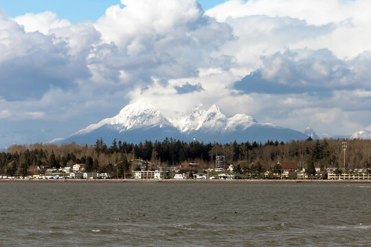 Wide view of Blaine, Washington, with snow capped Mount Baker and large puffy white clouds and calm water on a beautiful spring day.
