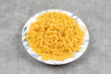 Plate of raw fusilli on marble surface