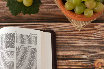 Open Holy Bible Book with fresh ripe grapes in a bowl placed on a wooden table with copy space....