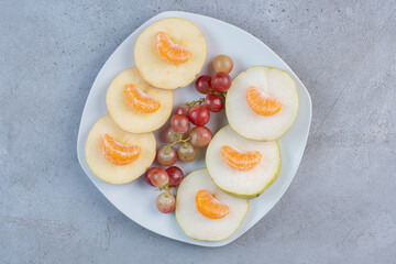 Sliced apples, pears, tangerines and grapes on a platter on marble background