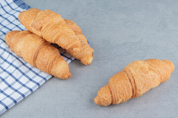 Three croissants stacked on the towel with a croissant on the marble background