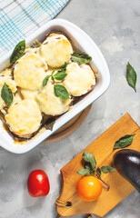 Eggplant baked with mozzarella cheese, tomatoes in baking dish on concrete table. Vegetarian food recipe
