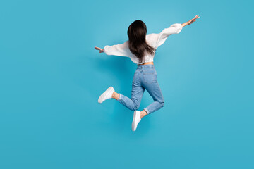 Full size rear behind photo of overjoyed active girl arms wings flying jump isolated on blue color background