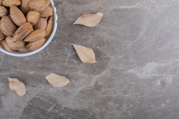 almonds in a bowl and leaves on the marble background
