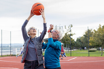 Senior couple man and woman play with baskett ball and have fun