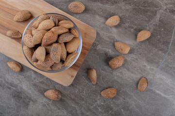A bowl of almonds on a tray and scattered almonds on the marble background