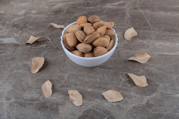 almonds in a bowl and leaves on the marble background
