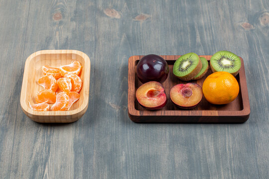 Sliced Fresh Kiwi With Orange And Plum On A Wooden Board