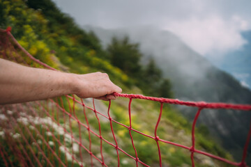 a man holds his hand to a red safety net on a mountain trail