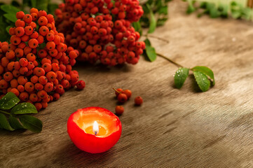 Autumn still life of a branch with red rowan berries and a red candle on a rough wooden background