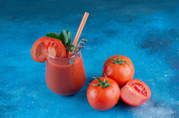 one glass tomato juice and two piece tomatoes on the blue background