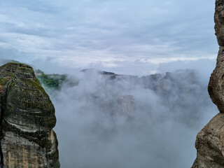 Scenic view of Holy Monastery of Varlaam, Kalambaka, Meteora, Thessaly, Greece, Europe. Monastery of Rousanos appearing from the fog, mystical atmosphere. Rock formations overgrown with green moss