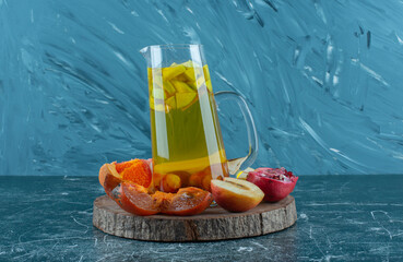 fruit slices on a board with natural juice in a carafe juice and apple on the blue background
