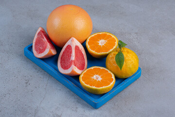 Whole and sliced tangerines and grapefruits on a small, blue tray on marble background