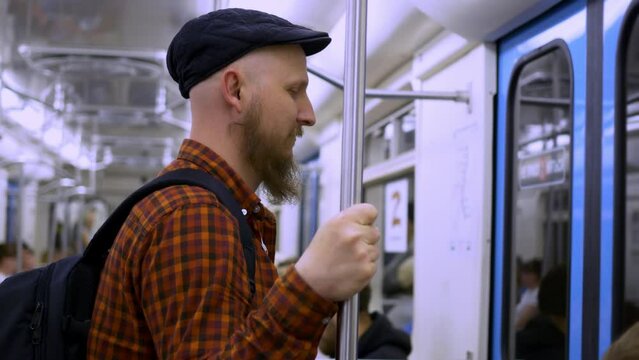 Side view of a bearded man in a cap with a backpack standing in a subway car. Simple life in public transport, trips to work on the subway. The man travels by public transport.