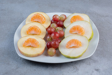 Sliced apples, pears, tangerines and grapes on a platter on marble background