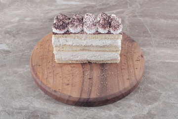 Cream and cocoa powder topped cake slice on a board on marble background