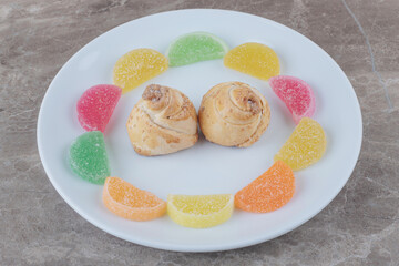 Marmelades around tiny cakes on a platter on marble background