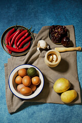 Still life with a bowl of raw eggs, raw potatoes, garlic in a wooden mortar, dried peppers and red hot peppers