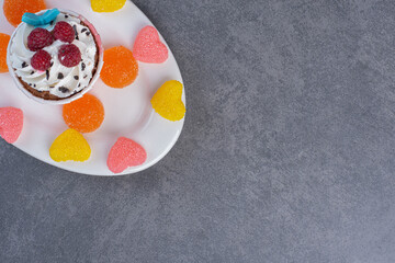 Tasty cupcake decorated with cream and raspberries on white plate
