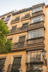 Obraz premium Old houses with vintage retro wrought iron metal balconies with color patterns on an old brick building with glass windows and leafy trees in the streets of the historic center of Madrid