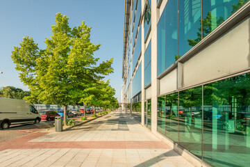 Glass, granite and metal facades in a street with young and leafy trees