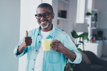 Photo of positive aged man hold caffeine beverage make thumb up symbol enjoy good quality arabica...