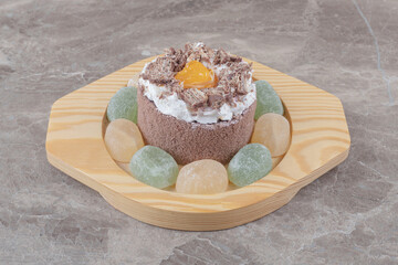 Marmelades around a small cake on a wooden platter on marble background