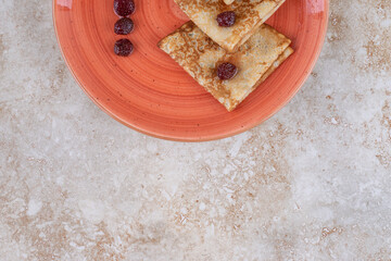 A orange plate with tasty thin pancakes and berries