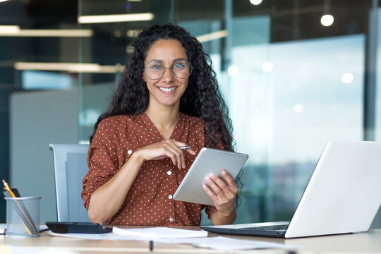 Happy and successful hispanic woman working inside modern office building, business woman using tablet computer smiling and looking at camera worker doing paperwork.
