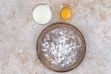 A brown plate of flour and a glass cup of milk