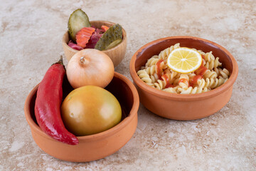 A clay bowl of delicious pasta with various vegetables