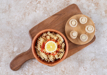 A wooden cutting board with mushrooms and spiral pasta