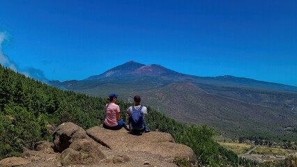 Sitting couple with scenic view on volcano Pico del Teide surrounded by pine tree forest, Teno mountain, Tenerife, Canary Islands, Spain, Europe. Hiking trail from Santiago to Masca via Pico Verde