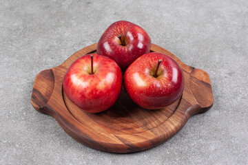 Three red apples on wooden board