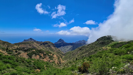 Panoramic view on the Teno mountain massif seen from summit Pico Verde, Tenerife, Canary Islands, Spain, Europe. Hiking trail between Masca and Santiago. Clouds over lush green hills. Tropical climate