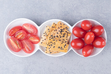 Serving platter with piles of tomatoes and sliced bread with sesame topping on marble background