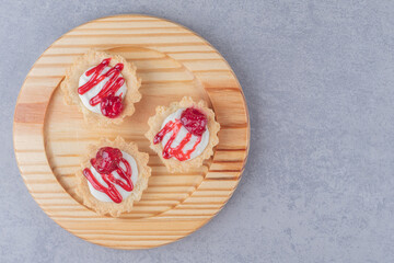 Cupcakes with strawberry syrup topping on a wooden platter on marble background
