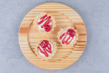 Cupcakes with strawberry syrup topping on a wooden platter on marble background